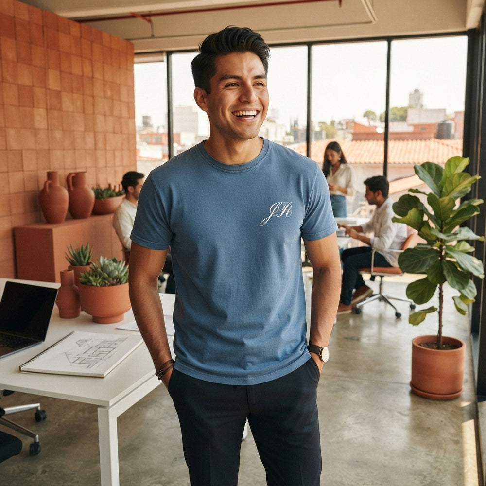 A young Mexican professional wearing a casual denim-colored cotton t-shirt in a modern office with terracotta decor.