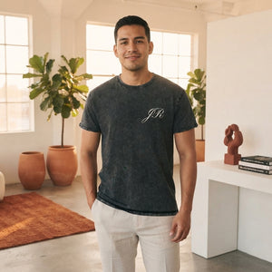 A confident Latino man wearing a high-quality denim-colored crew neck t-shirt in a modern, warm-toned studio setting.
